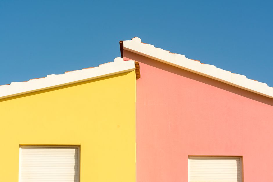 Close-up of vibrant yellow and pink house facades under a clear blue sky.