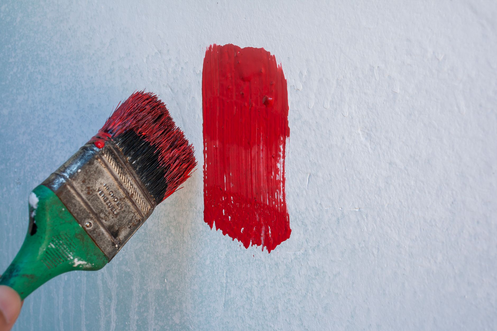A paintbrush applying red paint to a wall